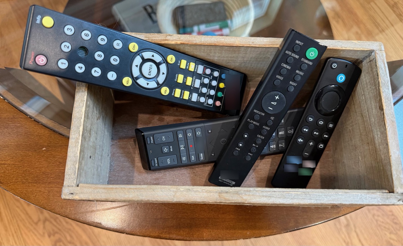 Five branded TV remotes in a wooden box